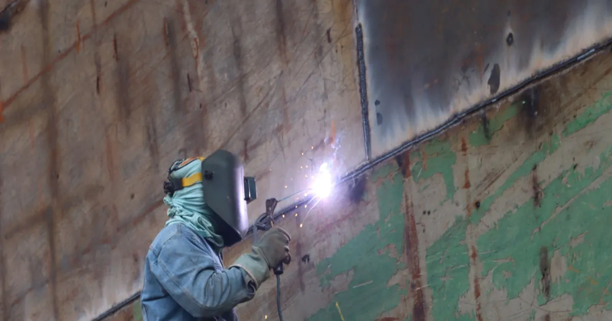 Welder working on a large steel plate in a fabrication shop, the kind of work behind an A36 or A572 machine base