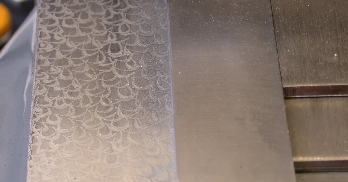 Close-up of a machine slideway with a hand-scraped flake pattern on one face and a plain machined face beside it