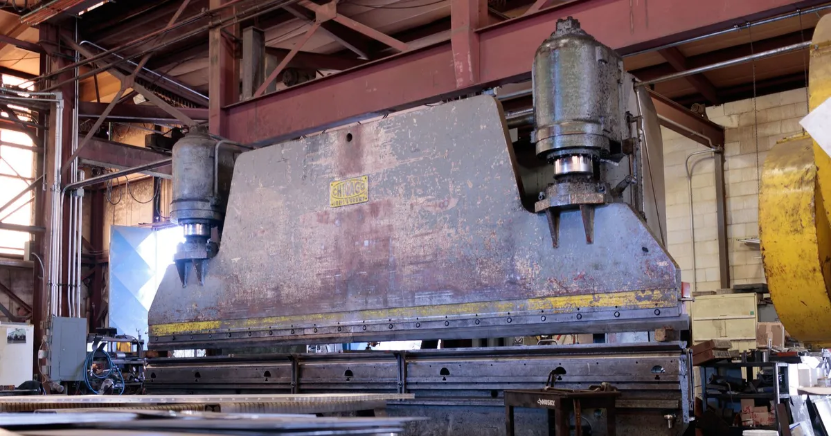 Large metal-forming press with a heavy welded steel frame in a workshop, hydraulic press frame fabrication